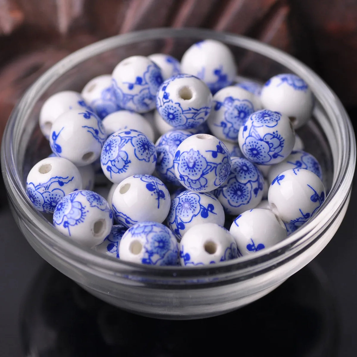 A clear glass bowl filled with white and blue floral ceramic beads for jewelry making