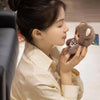 A woman holds a plush pendant featuring designs of a rabbit, bear, and sheep in soft brown and gray tones.