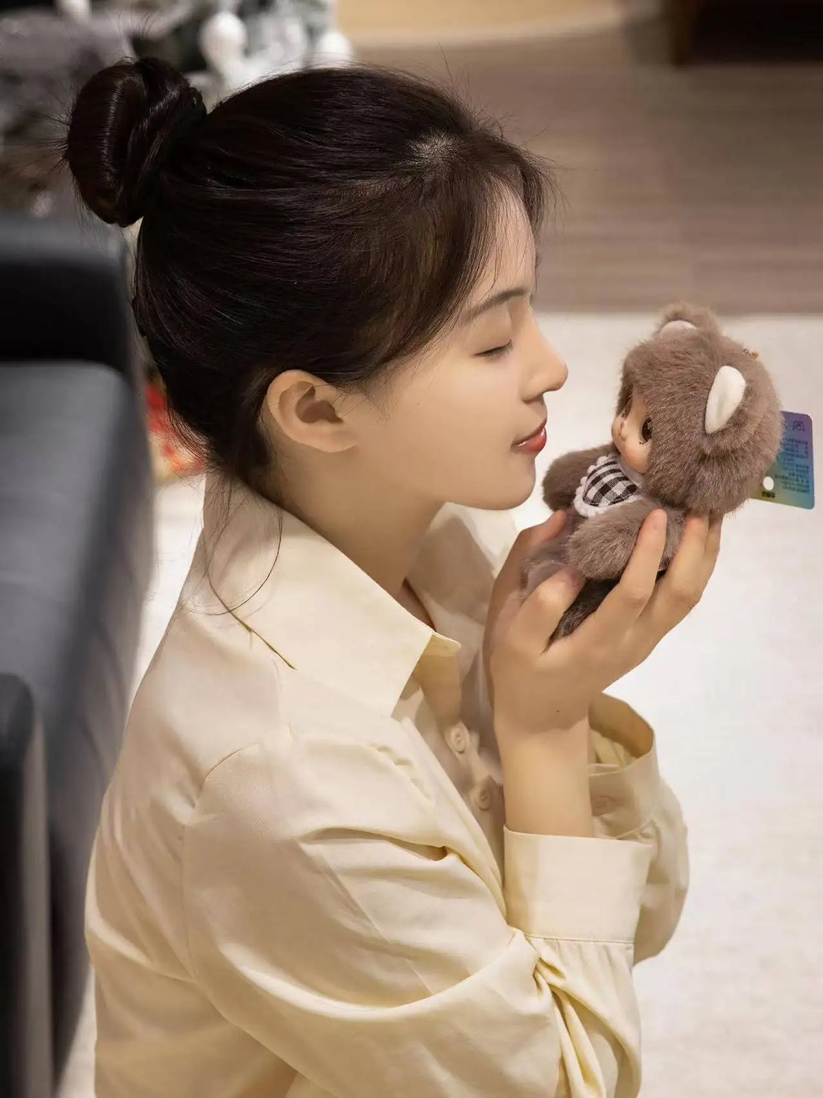A woman holds a plush pendant featuring designs of a rabbit, bear, and sheep in soft brown and gray tones.