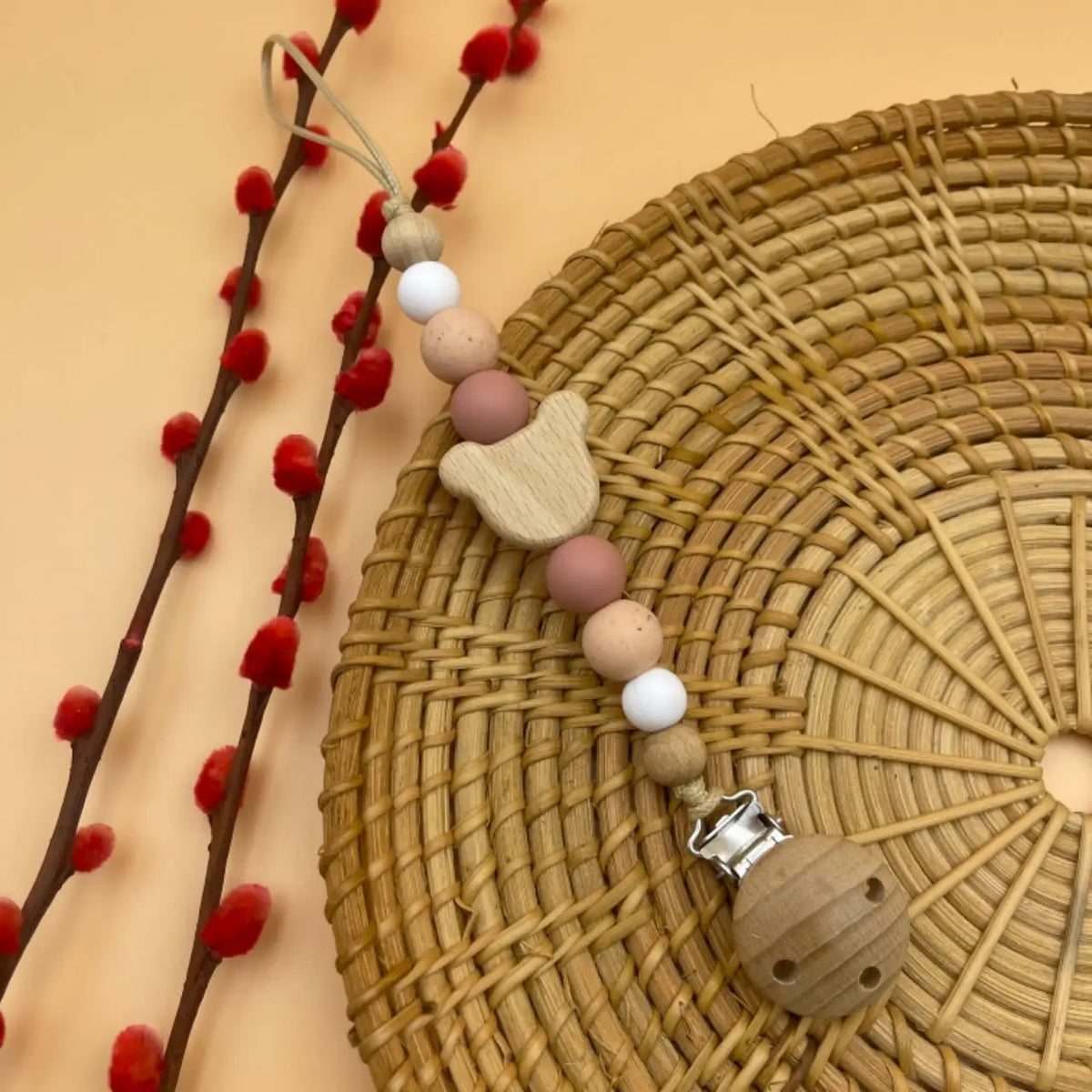 A string of wooden and silicone beads is displayed on a woven mat next to red berries.
