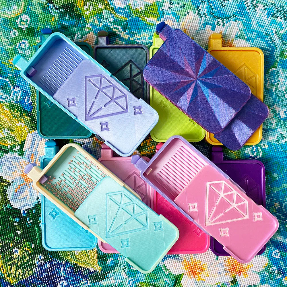 A collection of diamond painting organizer trays in various colors including purple, yellow, pink, and blue, arranged on a fl