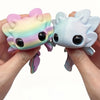 Two pastel colored flexible salamander figurines are held in a person's hands.