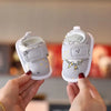 A pair of white soft sole first walker shoes with bear designs being held by a person's hands.