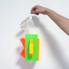 A hand is holding a clear plastic bag containing three colored molds for building sand and snow structures.