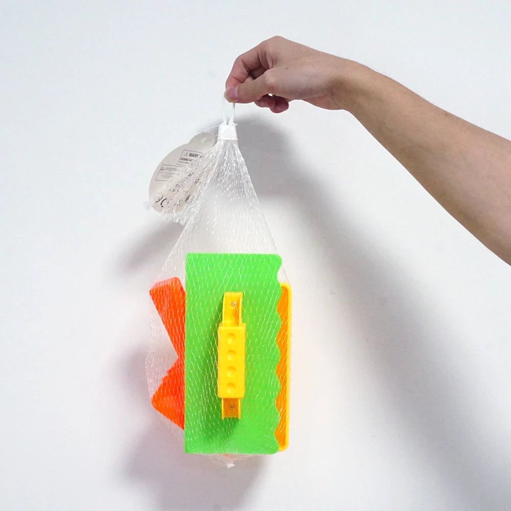 A hand is holding a clear plastic bag containing three colored molds for building sand and snow structures.