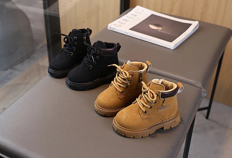 A pair of tan leather winter boots with laces and a side zipper resting on a gray table next to a book.