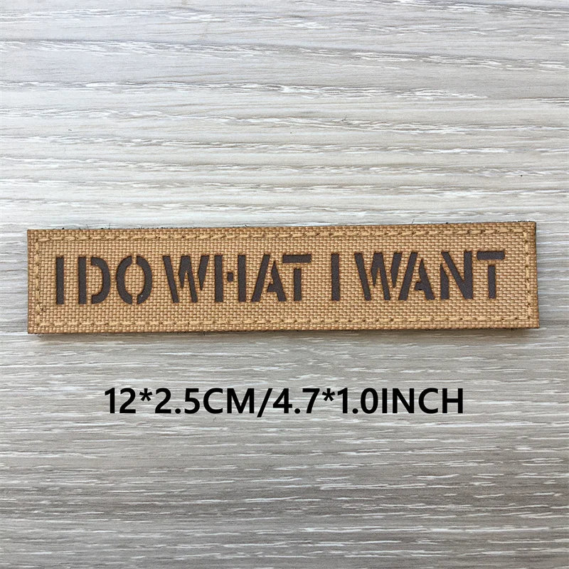 Un patch tissé brun rectangulaire avec le texte ID WHAT I WANT sur une surface en bois clair.