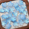 A collection of light blue maple leaf glass beads arranged on a white surface.