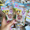 A hand holds a Sylvanian Families blind bag collectible figure package featuring a yellow-eared animal character.