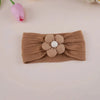 A brown knitted floral elastic baby headband with a white center flower resting on a light pink background.