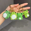 A hand holds several handmade crochet frog keychains with green and white yarn, featuring metal clasps.