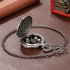 A silver steampunk dragon pocket watch dice case with a textured lid and a chain is displayed on a brown leather surface.