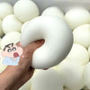 A hand is holding a large, white squishy bread stress ball among many similar white balls.