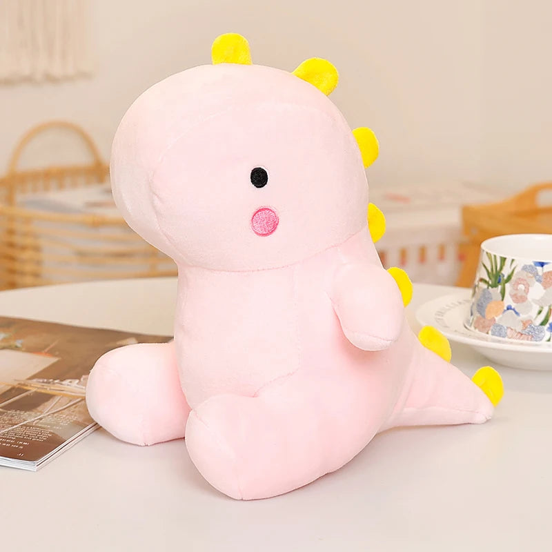 A pink dinosaur plush toy with yellow spikes and a pink nose sitting on a white surface.
