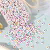 A pile of colorful letter and number acrylic beads scattered on a light blue surface with a clear container nearby.