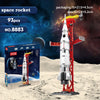 A white space rocket model is displayed on a red stand, next to its packaging and building blocks.