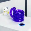 A purple crystal fidget twist rope is stacked on a white surface next to a white and yellow bear toy.