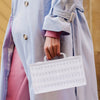A hand holds a clear plastic multi-compartment storage organizer for beads and craft supplies, worn under a light blue coat.