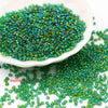 A pile of glossy green seed beads scattered on a white dish and surrounding surface.