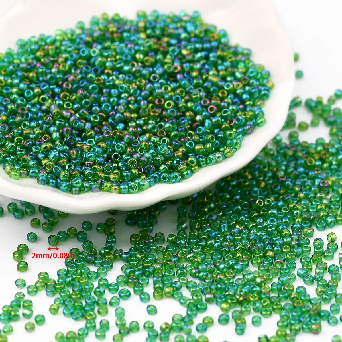 A pile of glossy green seed beads scattered on a white dish and surrounding surface.