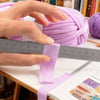 A hand measures a purple soft chunky t-shirt yarn skein against a ruler.
