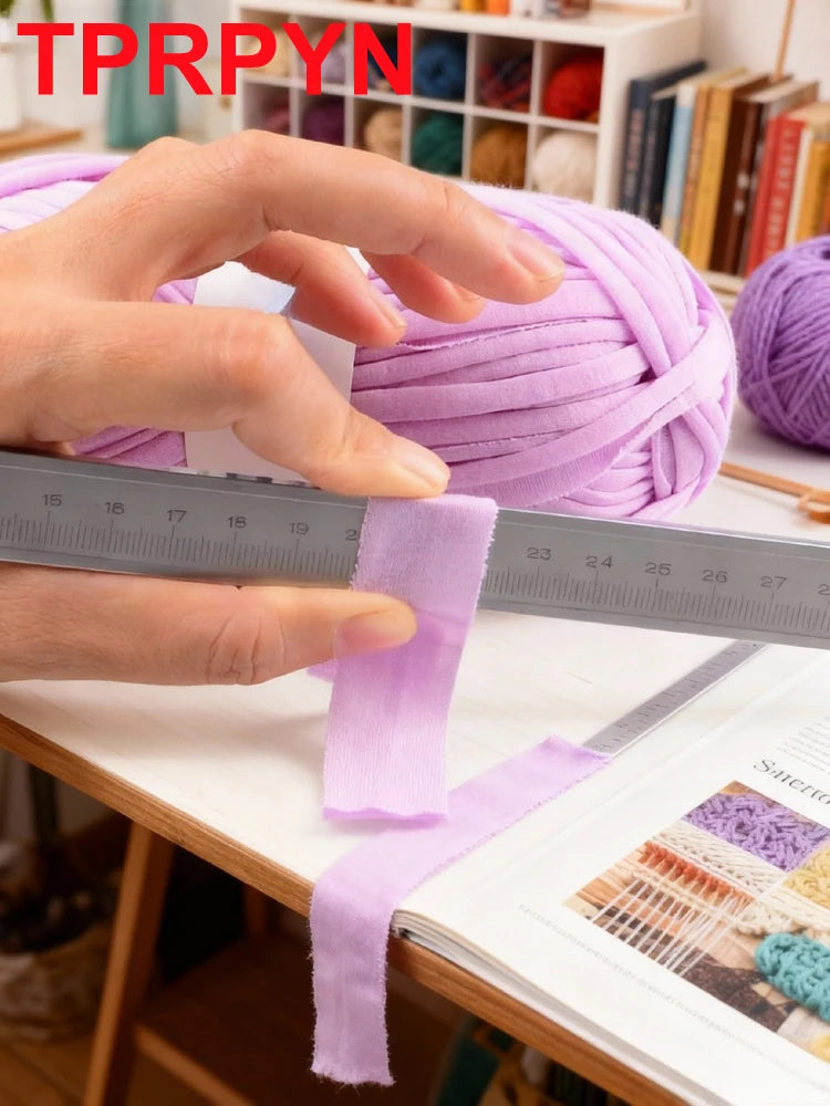 A hand measures a purple soft chunky t-shirt yarn skein against a ruler.