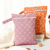 Two reusable pink and orange waterproof baby wet bags resting on a white surface with a cream knit blanket.