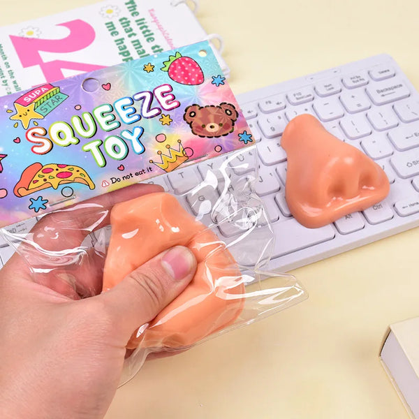 A hand holds an orange squeeze toy fidget tool next to a keyboard and a colorful toy box.
