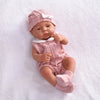 A lifelike vinyl reborn doll wearing a pink knitted outfit and matching hat, lying on white fabric.