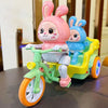 A pink rabbit plush toy is seated on a green electric tricycle with yellow accents.