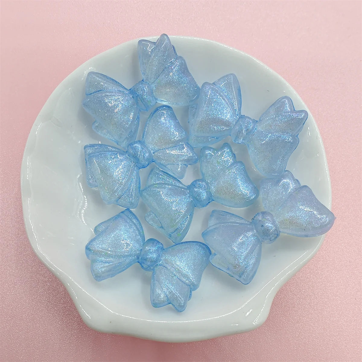 A collection of shimmering light blue mermaid bowknot beads arranged on a white dish.
