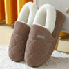 A pair of taupe knitted slippers with white faux fur lining resting on a white surface.