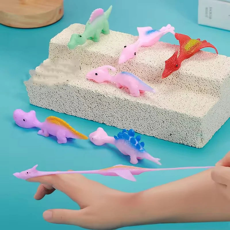A hand is holding a pink rubber dinosaur toy, with several other colored dinosaurs arranged on a white foam block.