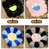 Four variations of large sunflower plush cushions in black, pink, blue, and gray.