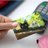 A hand holds a card featuring cute black and white cat illustrations on a green leafy background.