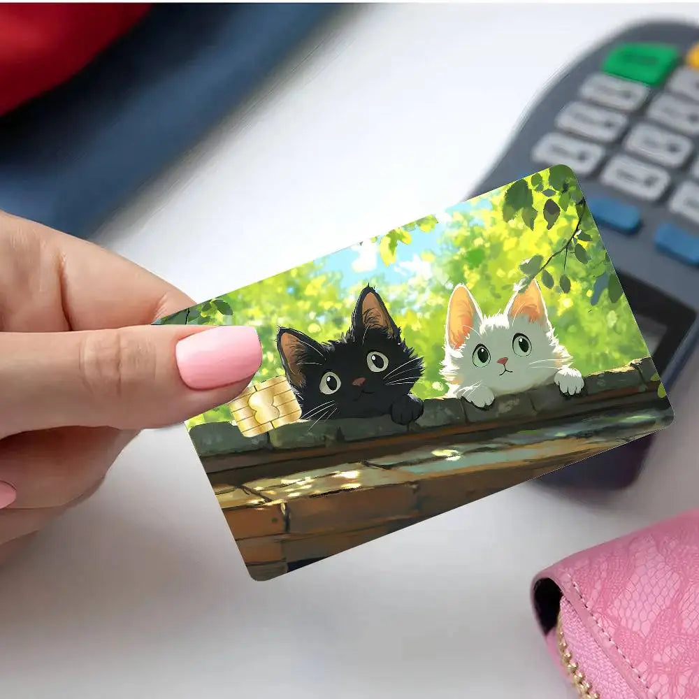 A hand holds a card featuring cute black and white cat illustrations on a green leafy background.