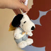 A white Snoopy plush keychain charm is being held by a hand against a blurred orange and blue background.