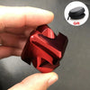 Une main tient un cube jouet à faire tourner en alliage rouge brillant, avec une pochette cadeau noire à proximité.