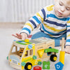 A young child is playing with a wooden toy vehicle set that includes tools and building pieces.