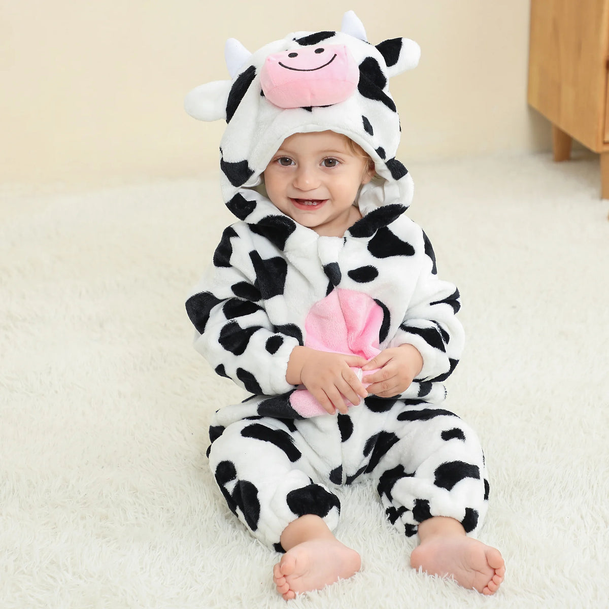 A baby wearing an adorable animal hooded romper with a white and black cow print face mask