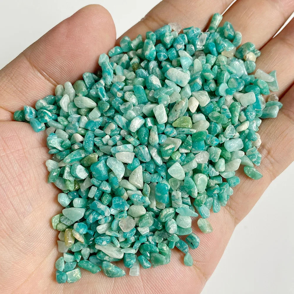 A hand holds a pile of bright turquoise green natural tumbled stone chips for jewelry making and home decor.