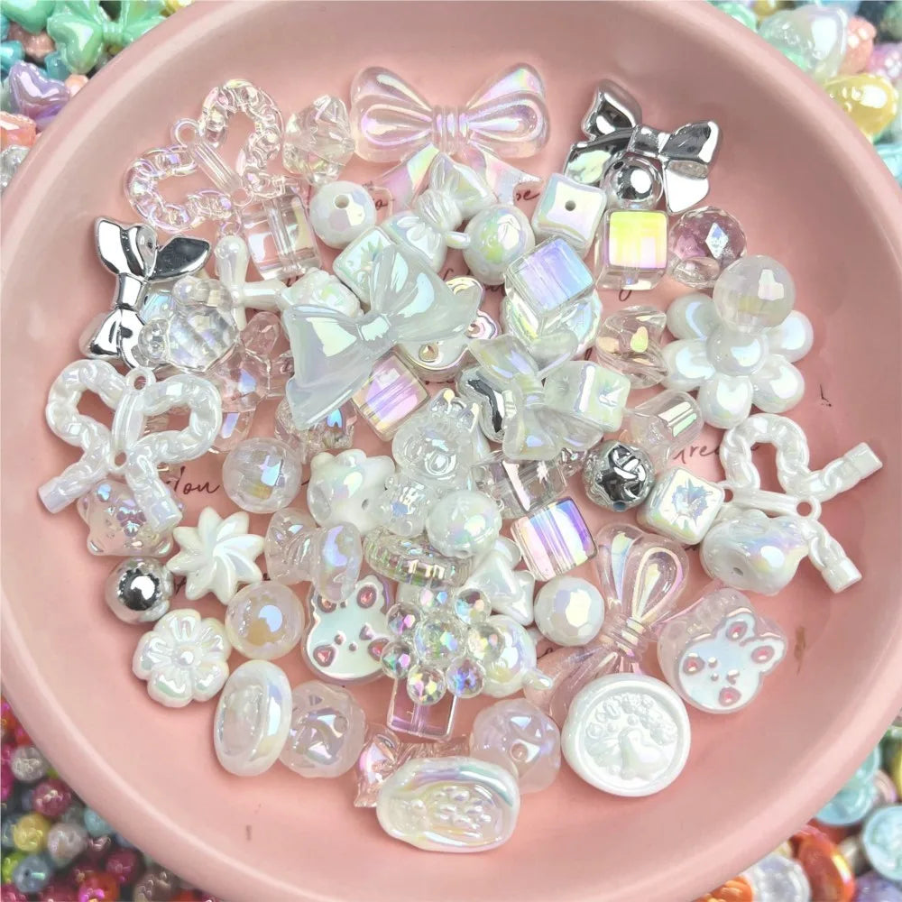 A collection of clear and iridescent acrylic bow and flower beads for DIY jewelry making displayed in a pink bowl.