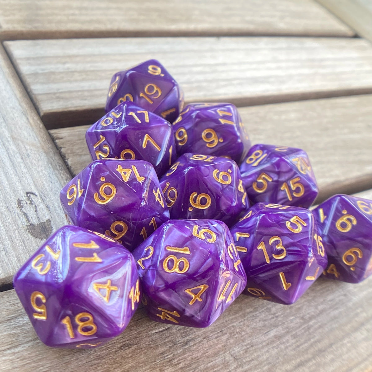 A collection of ten purple pearl acrylic D20 dice arranged on a wooden surface.