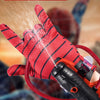 A hand wearing a red patterned glove is launching a stream of water from an orange wrist launcher.