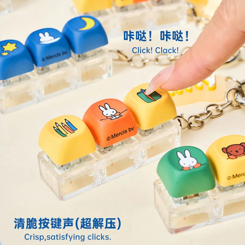 A hand is shown pressing a yellow keycap pendant onto a clear plastic base, demonstrating a crisp clicking sound.