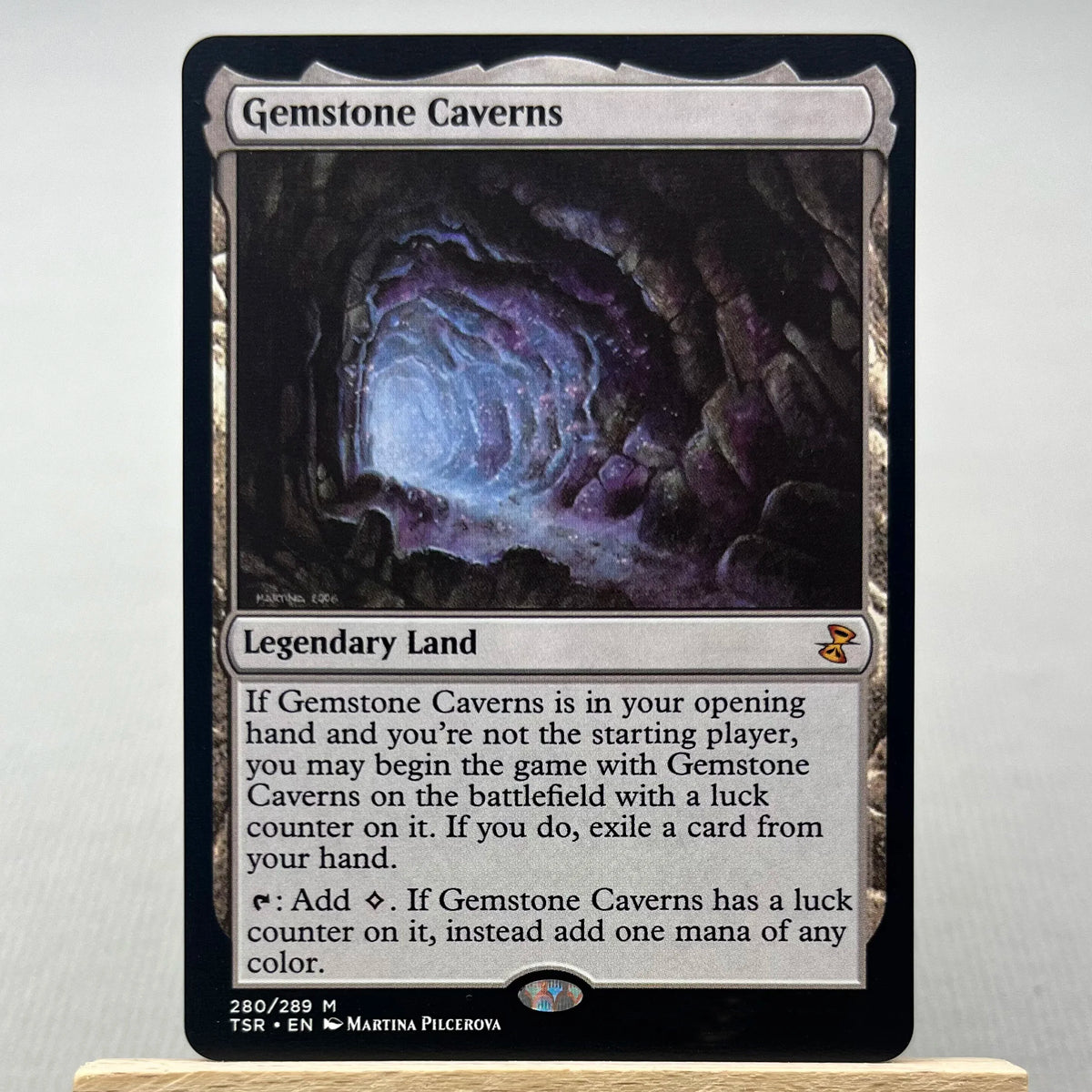 A Magic: The Gathering card named Gemstone Caverns showing a dark cavern landscape