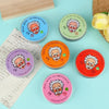 A collection of six round glass containers of slime with various facial expressions and colors arranged on a light blue surfa