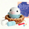 A beginner bird crochet kit featuring a white and light blue amigurumi figure, yarn, and a purple packaging bag.