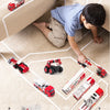 A child is playing with a die-cast fire fighting vehicle set featuring various trucks and a ladder truck on a carpeted floor.