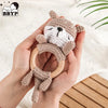 A hand holds a wooden otter rattle and teether ring made of soft beige fabric with a bear face detail.